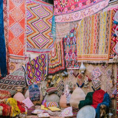 Colorful handmade carpets and pottery on display in a traditional market setting.