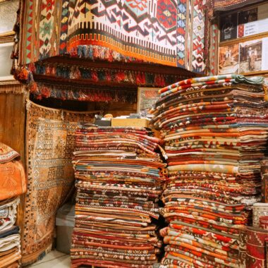 Stacks of vibrant Turkish carpets on display in an Istanbul bazaar, showcasing intricate designs.