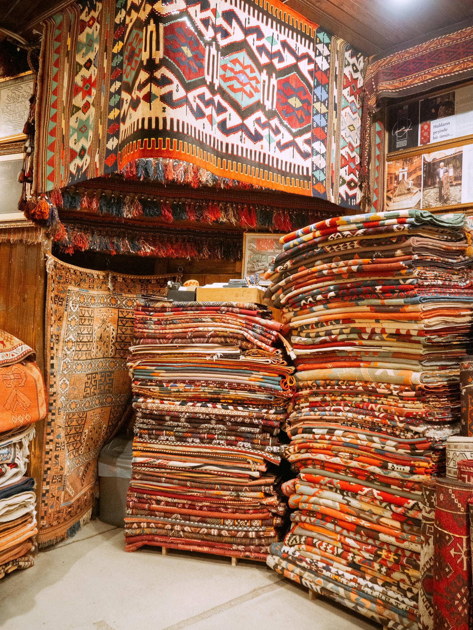 Stacks of vibrant Turkish carpets on display in an Istanbul bazaar, showcasing intricate designs.